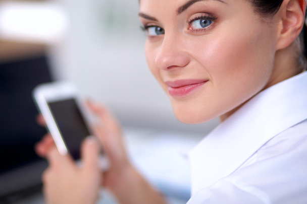 Businesswoman sending message with smartphone sitting in the office - Фото, зображення