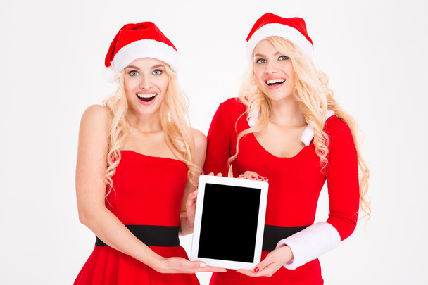 Cheerful women in santa cloth showing tablet computer screen  - 写真・画像