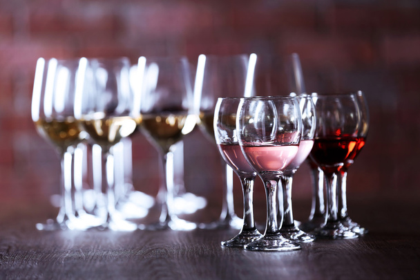 Wineglasses with white, red and pink wine on wooden table on wall brick background - Valokuva, kuva
