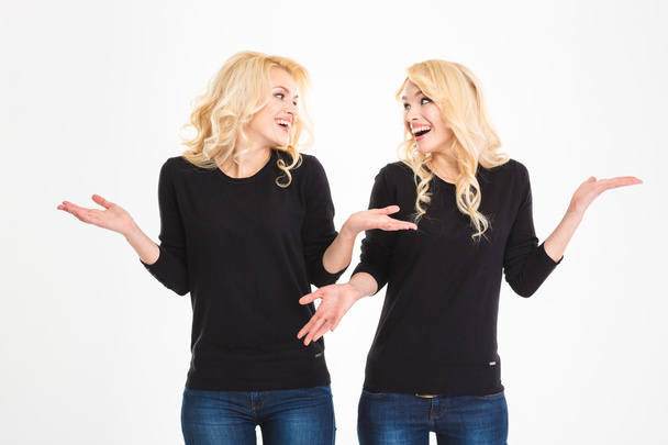 Laughing sisters twins looking at each other and shrugging shoulders - Fotoğraf, Görsel