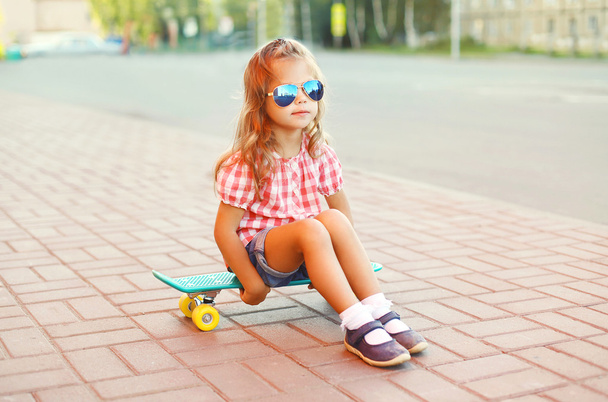 Elegante bambina seduta sullo skateboard indossando una sungla
 - Foto, immagini
