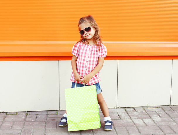 Child wearing a sunglasses with shopping bags walking in city - Foto, Imagem