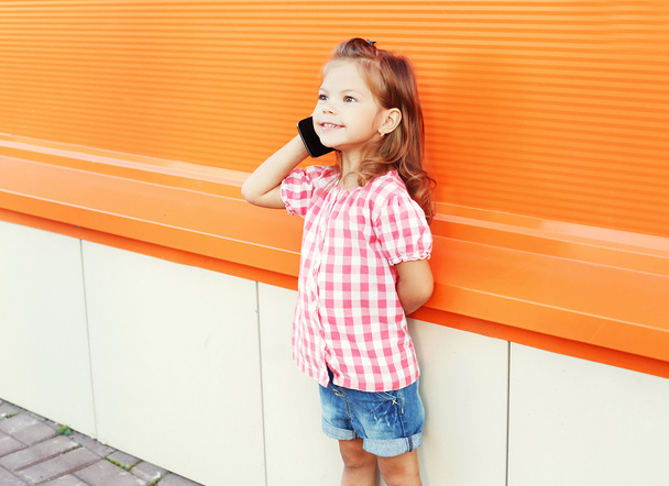 Happy smiling little girl child talking on smartphone in city - Foto, Bild