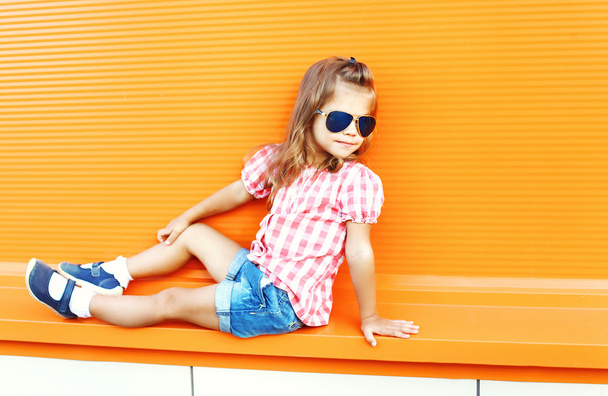 Stylish child wearing a sunglasses and checkered shirt in city - Foto, imagen