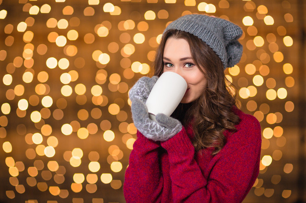 Beautiful woman in grey hat and mittens drinking hot chocolate  - Foto, afbeelding