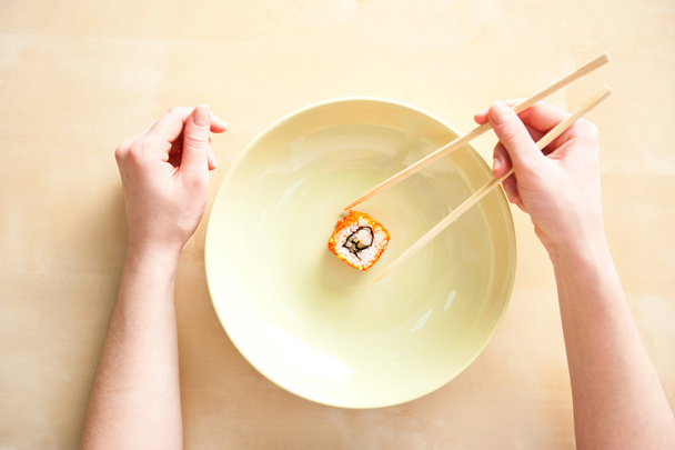 Woman holding sushi with chopsticks top view - Фото, изображение
