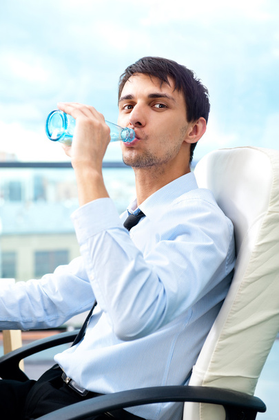 Young business man drinking water sitting relaxed on armchair at his modern office - Foto, Imagen