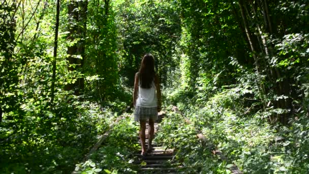 Nastolatek dziewczyna spacery po malowniczej linii kolejowej z zielonych drzew wokół - Materiał filmowy, wideo