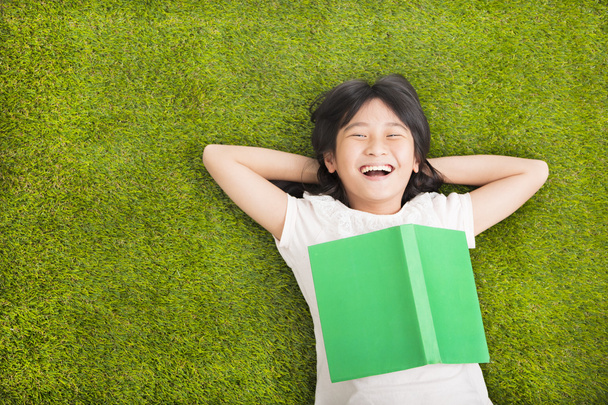 onnellinen pieni tyttö kirjan kanssa ja lepää ruohikolla
 - Valokuva, kuva