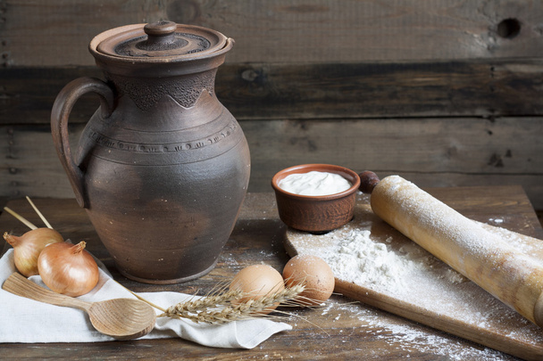 Rustic natural dairy products. Rustic natural dairy products sour cream in clay dishes, eggs and ears of wheat on the old wooden background. - Photo, Image