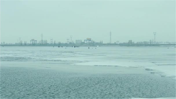 Winter anglers on ice on background of hydroelectric power plant - Materiał filmowy, wideo