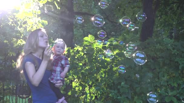 Beautiful mother and little baby daughter blowing soap bubbles together in evening sunlight. 4K - Footage, Video