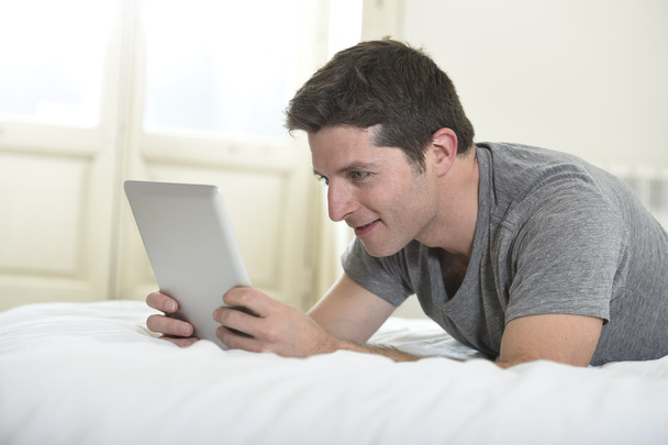 joven atractivo hombre acostado en la cama o sofá disfrutando de las redes sociales utilizando tableta digital de Internet en casa
 - Foto, imagen