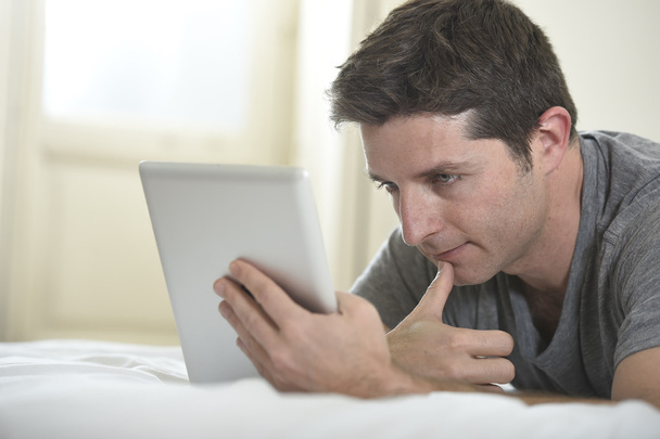 young attractive man lying on bed or couch enjoying social networking using digital tablet computer internet at home - Photo, Image