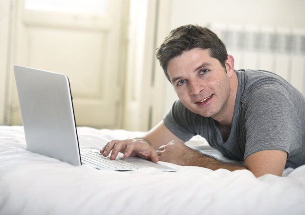 young attractive man lying on bed or couch enjoying social networking using computer laptop at home - Photo, image