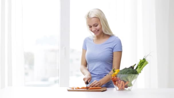 smiling young woman chopping vegetables at home - Imágenes, Vídeo