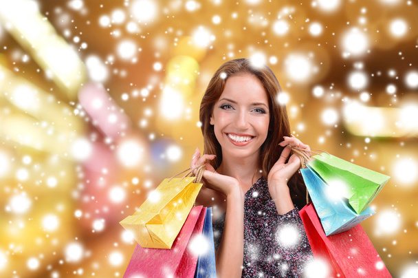 Beautiful young woman with shopping bags on bright background over snow effect - Foto, afbeelding