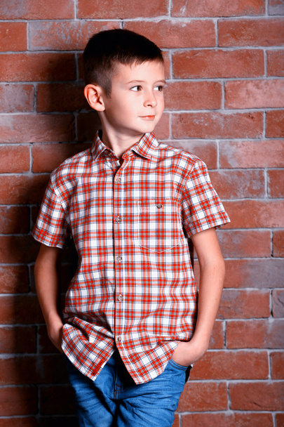 Cute little boy on brick wall background. Kids fashion concept - Фото, изображение