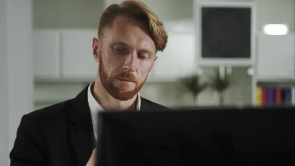 Red-haired man sitting at a computer and calling on the phone - Footage, Video