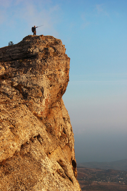 Чоловік стоїть на скелі і вказує далеко
 - Фото, зображення
