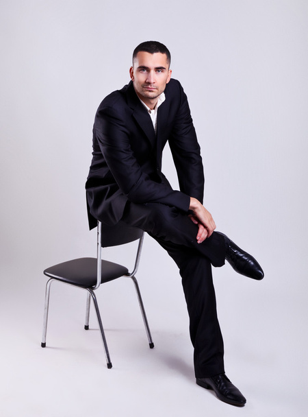 Elegant young businessman sitting on a chair over gray background - Foto, Imagen