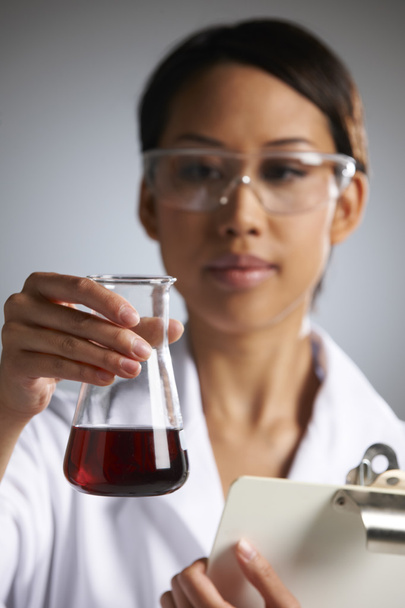 Scientist Examining Liquid In Flask Holding Clipboard - Foto, afbeelding