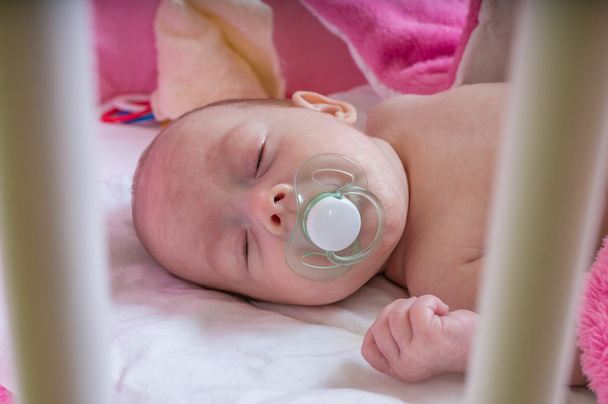 Спящий новорожденный за решеткой детской кроватки
 - Фото, изображение