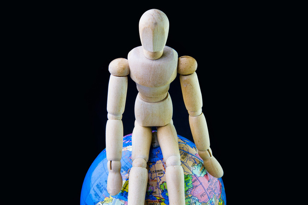 Wooden figure sit on a globe model. - Photo, Image