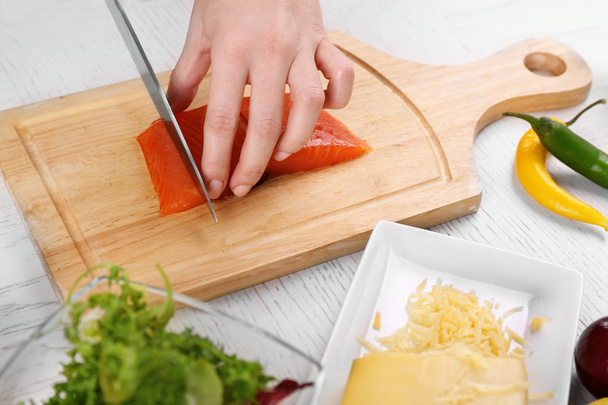 Woman cutting smoked salmon for salad, at kitchen - Foto, afbeelding