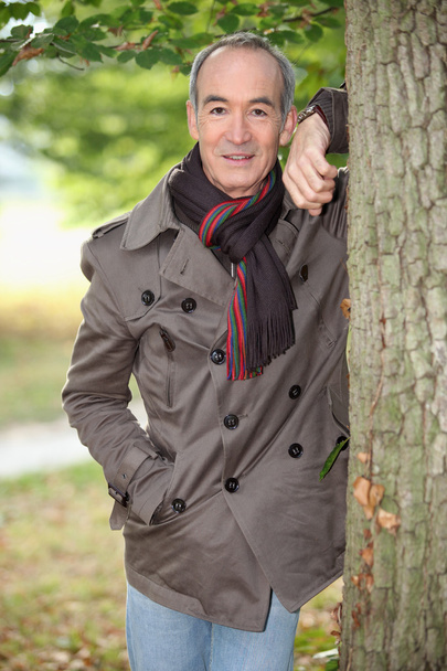 Senior man leaning against a tree - Foto, afbeelding