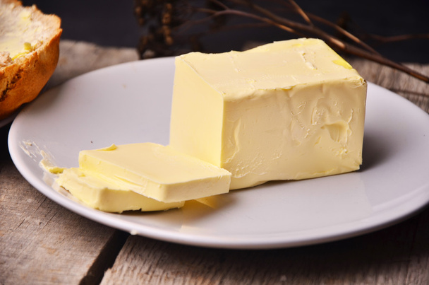 Pat di burro fresco di fattoria su un piatto di burro con un coltello da usare come ingrediente diffusione o coppettazione, vista aerea su un tavolo di legno a doghe
 - Foto, immagini