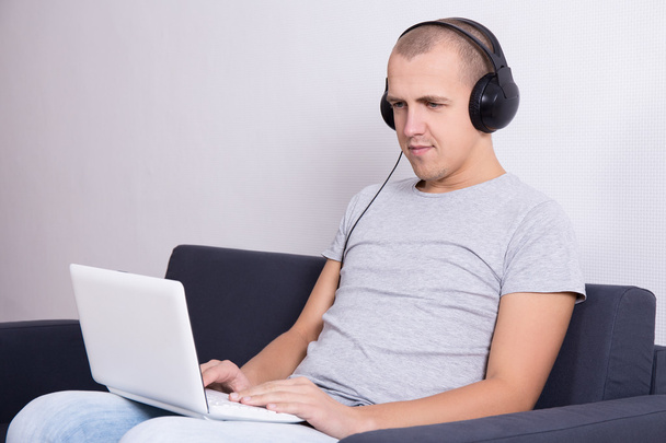 young handsome man sitting on sofa with computer and listening m - Foto, Imagem