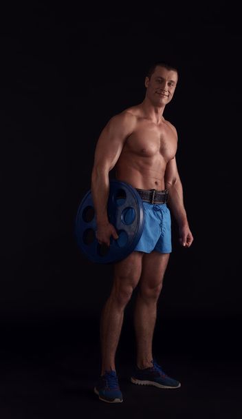 Handsome bodybuilder posing with barbell disk - Zdjęcie, obraz