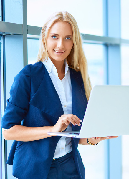 Businesswoman standing against office window holding laptop - Foto, Imagem