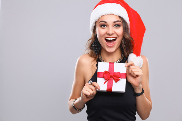 Woman in Santa hat holding gifts, isolated on gray - Photo, image