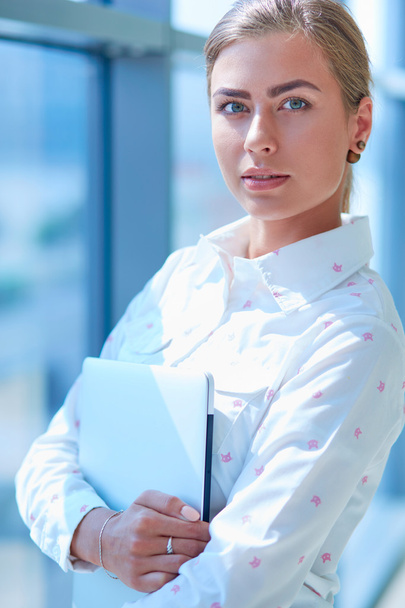 Businesswoman standing against office window holding documents in hand - Foto, imagen
