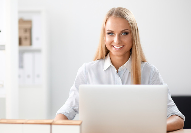 Attractive businesswoman sitting on a desk with laptop in the office - Foto, afbeelding
