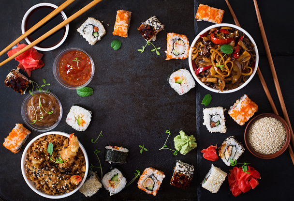 Traditional Japanese food - sushi, rolls, rice with shrimp and udon noodles with chicken and mushrooms on a dark background. - Fotoğraf, Görsel