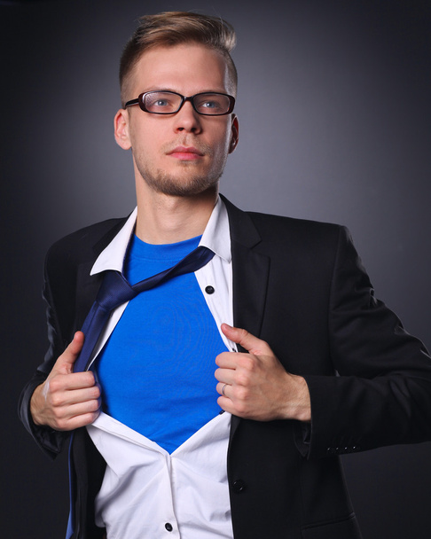 Joven hombre de negocios actuando como un súper héroe y rasgando su camisa, aislado sobre un fondo gris
 - Foto, imagen