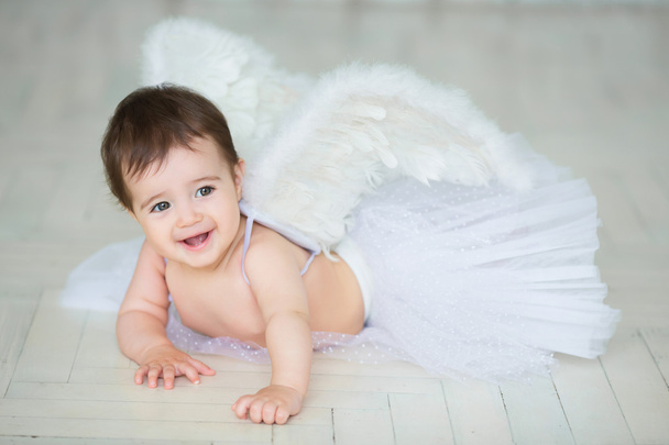 Portrait of a cute baby dressed in angel wings sitting and eating  carrot. - Fotografie, Obrázek