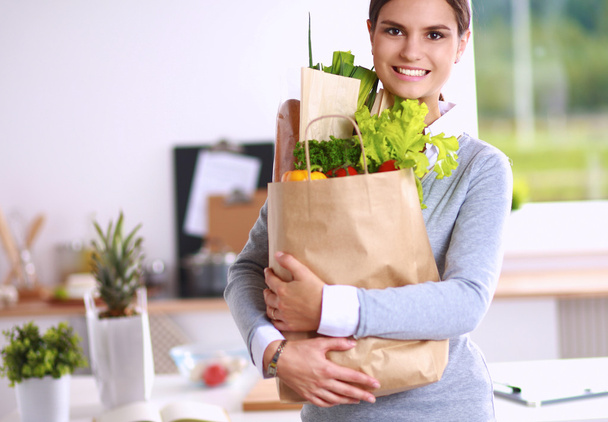 Young woman holding grocery shopping bag with vegetables Standing in the kitchen. - Photo, Image