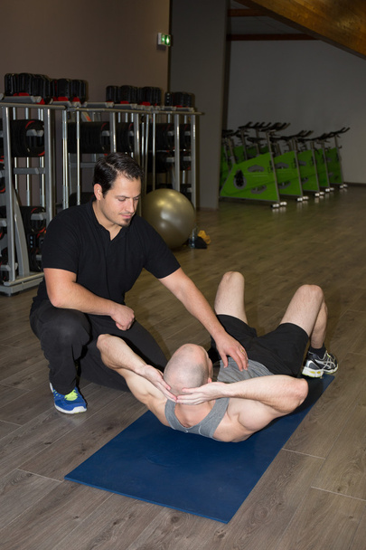 Male trainer assisting man with push ups in fitness studio - Foto, afbeelding