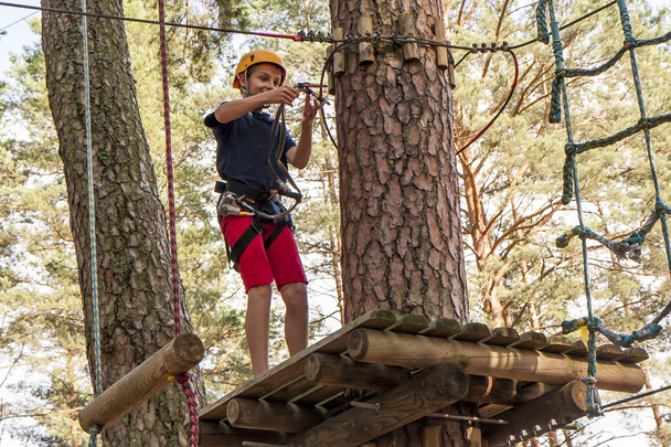 Um menino usando um cinto de segurança e um capacete andando em um parque de cordas
. - Foto, Imagem