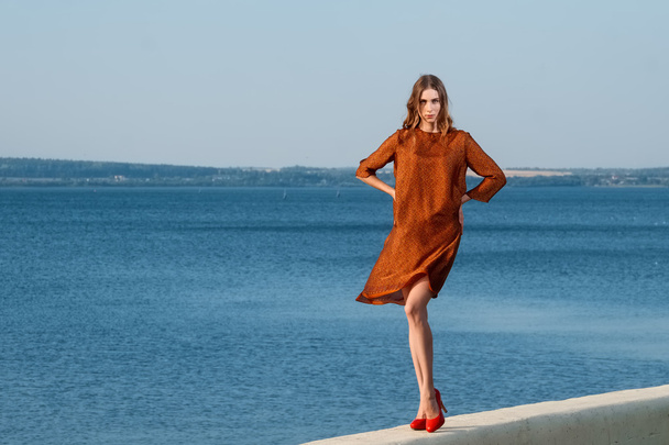 chica bonita en un muelle en vestido naranja con mar y barcos en el fondo
 - Foto, Imagen