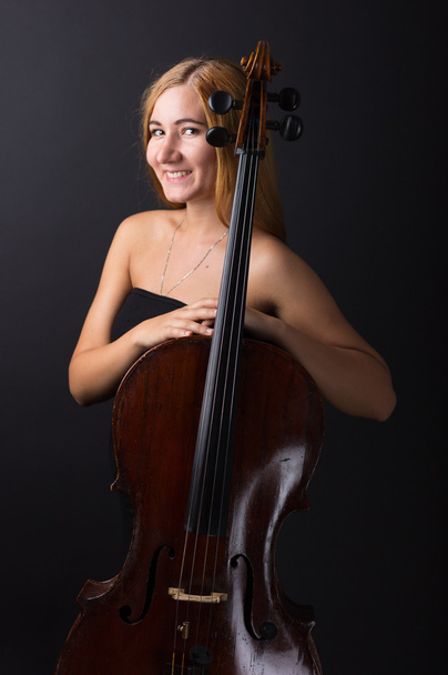 Beautiful girl with a cello on a black background. Cellist. Girl musician. - Фото, изображение