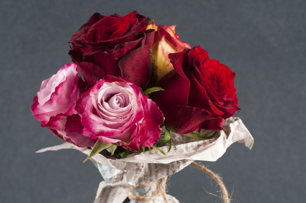 Bunch of multicolor rose flowers wrapped in newspaper over grey  - Foto, Bild
