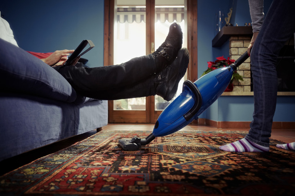 Hombre relajándose mientras mujer haciendo tareas en casa
 - Foto, Imagen