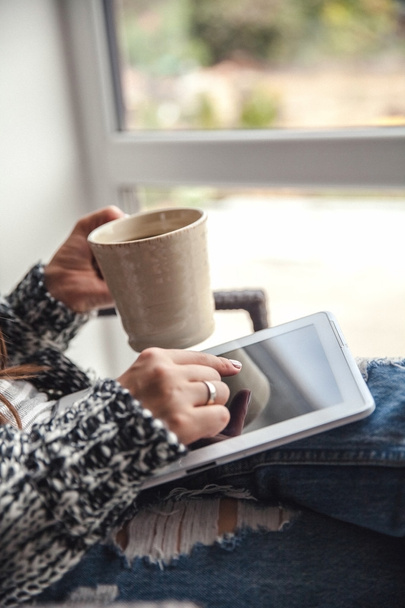 Soft photo of woman In the armchair with tablet and cup of coffee in hands, ripped jeans - Fotó, kép