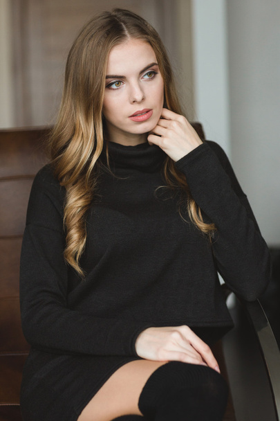 Gorgeous thoughtful woman in black dress sitting on leather sofa  - 写真・画像