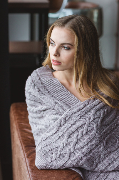 Thoughtful woman sitting on sofa wrapped in grey knitted coverlet - Foto, Bild